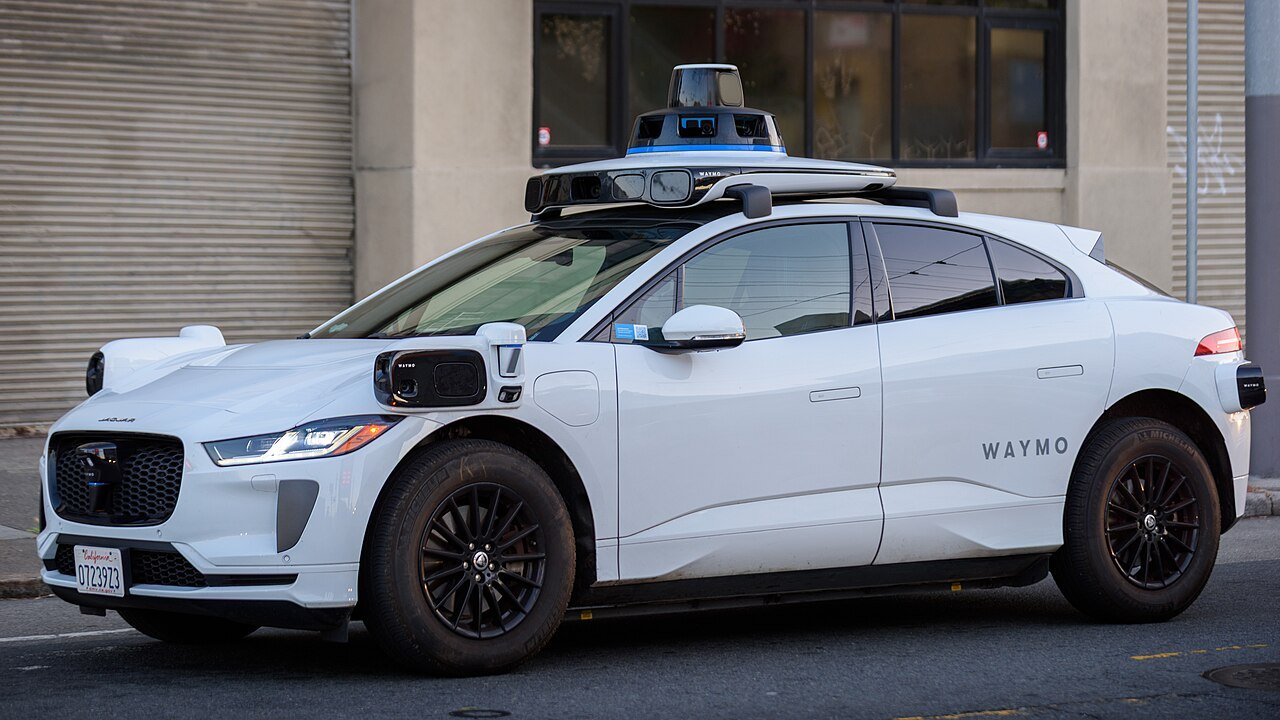 Waymo Jaguar I-PACE with autonomous-driving sensors — real San Francisco photograph used illustratively for the Munich expansion story