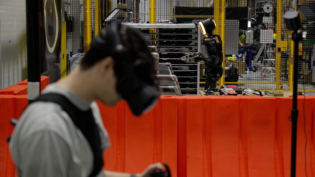 An operator wearing training equipment with an Atlas robot at Boston Dynamics’ RMAC