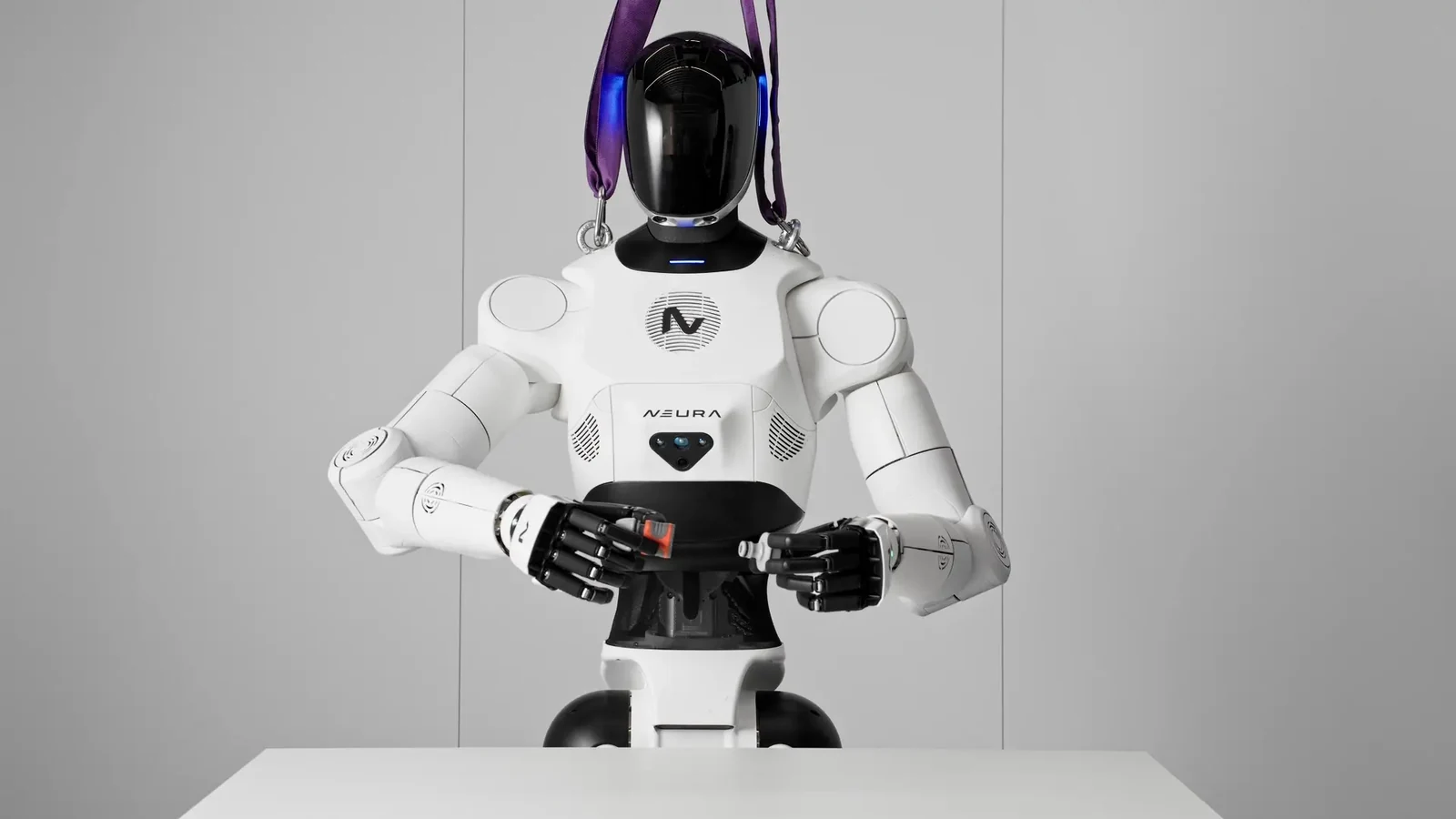 Humanoidalny robot NEURA przy stole, podtrzymywany fioletowymi pasami asekuracyjnymi, z elementami trzymanymi w dłoniach.